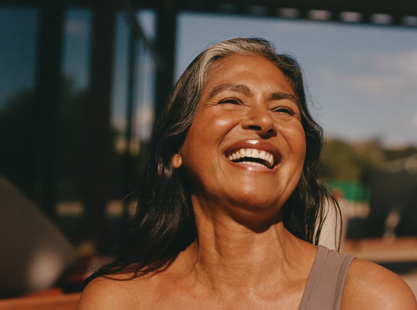 A woman in her mid fifties laughing on a sunlit terrace