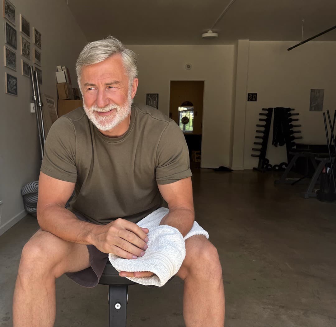 A man in his fifties resting on a bench in his home gym