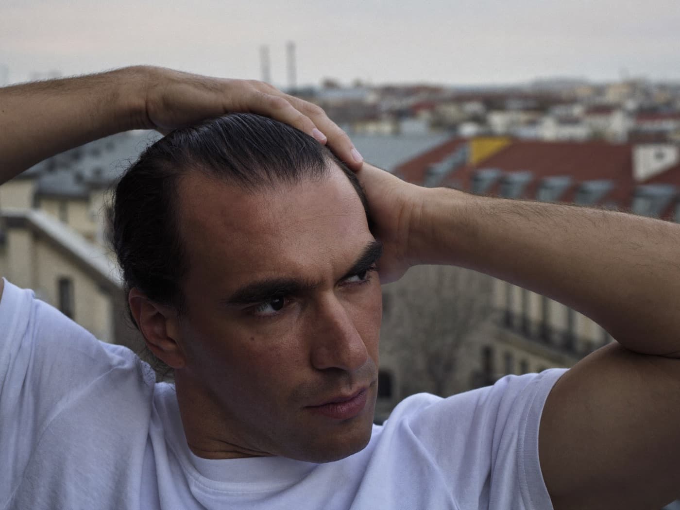 A man in his late thirties running his hands back through his hair on a city balcony
