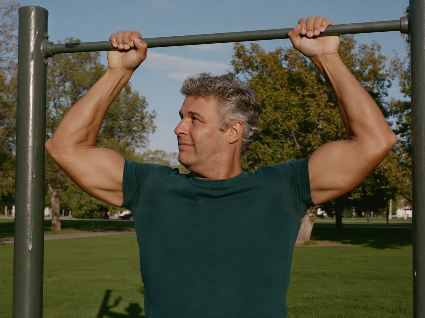 A man in his forties doing pull-ups on an outdoor bar in a park