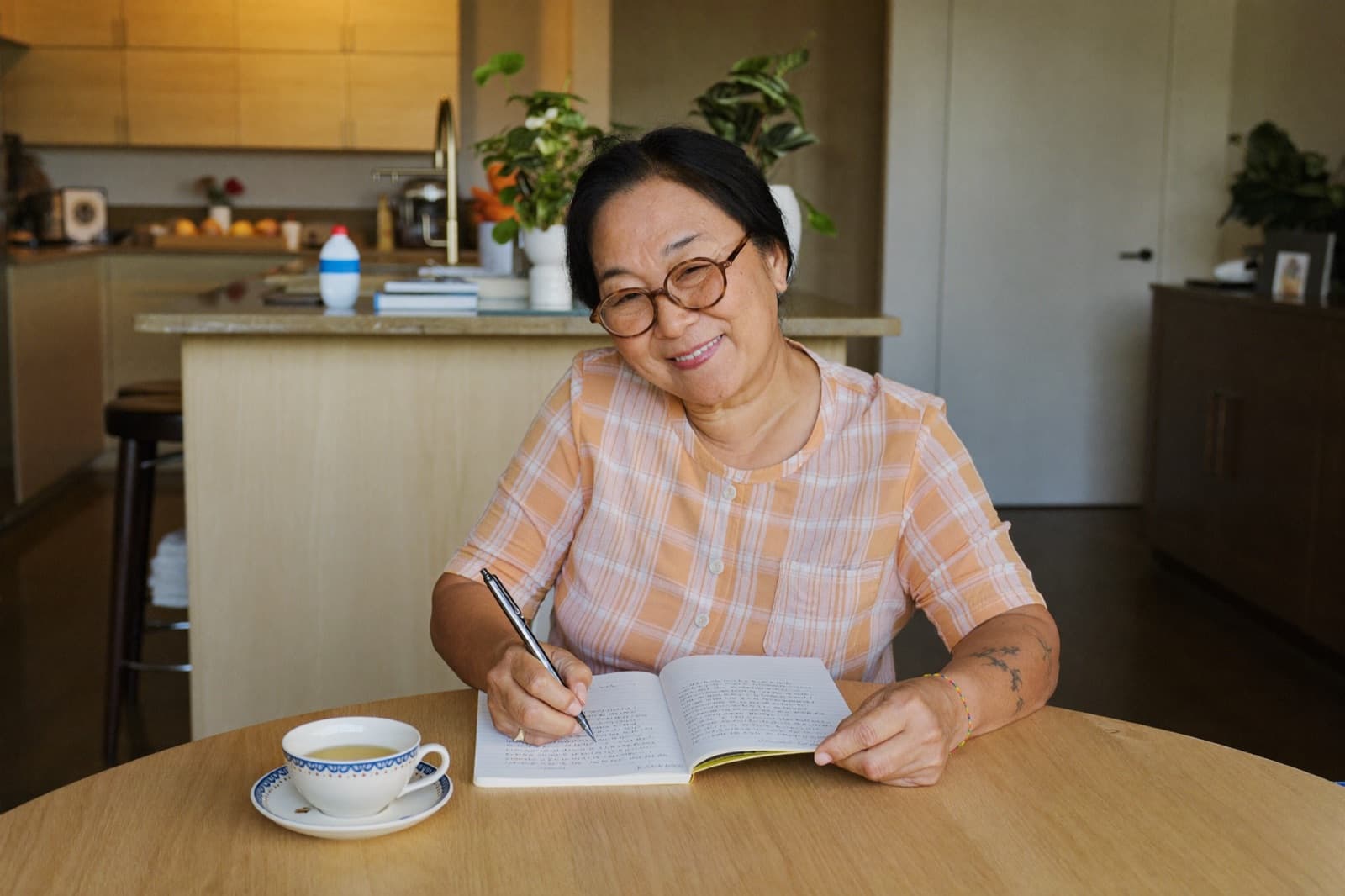 A woman in her fifties writing in a notebook at her kitchen table