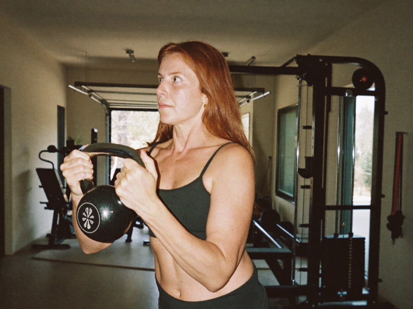 A woman in her forties with long auburn hair holding a kettlebell in a home gym