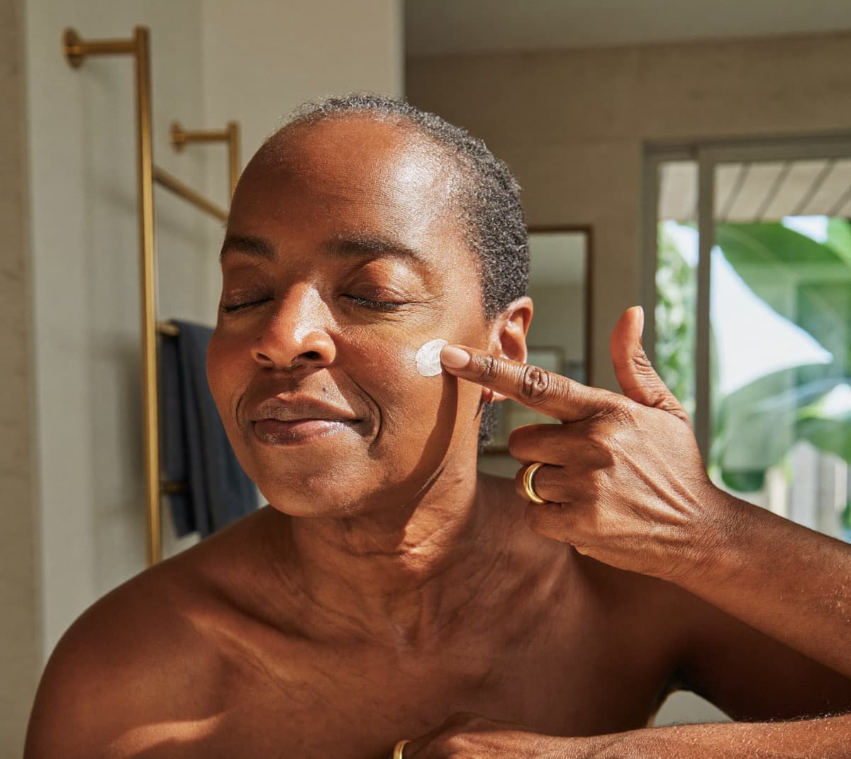 A woman in her fifties applying face cream in warm morning light